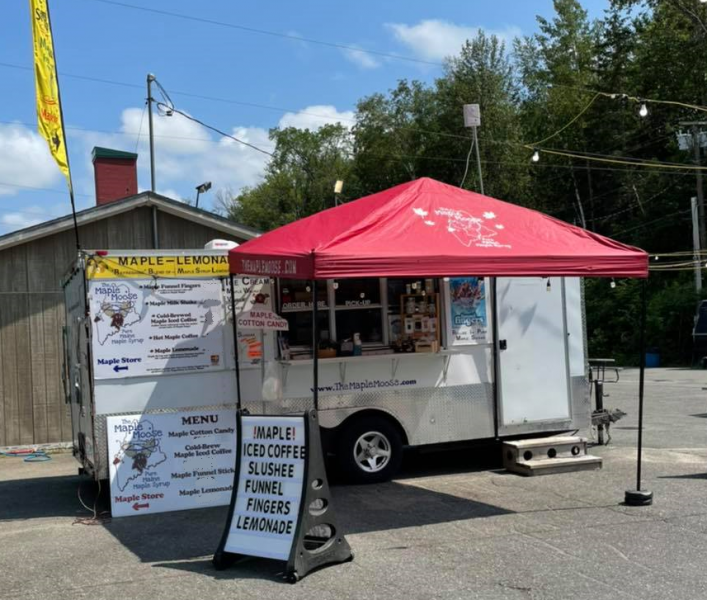 Food trailer with a red canopy selling maple lemonade, iced coffee, and funnel fingers.