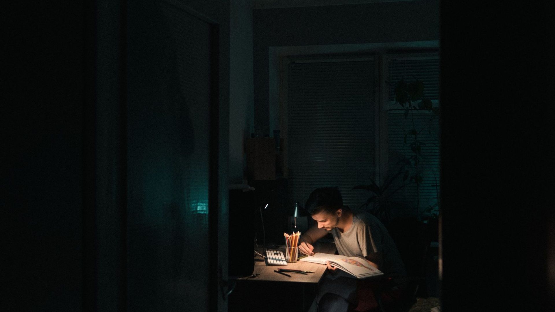 A person working alone at a desk in a darkened room late at night