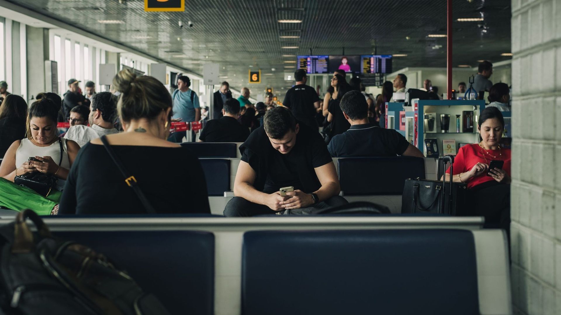 Travelers waiting at an airport gate, one of them reading a phone