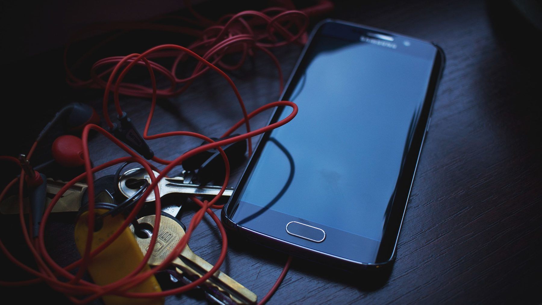 A phone and a set of house keys on a dark table