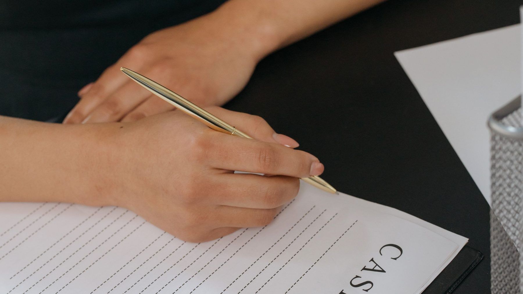 A hand writing on a case notepad beside a pen and a coffee cup