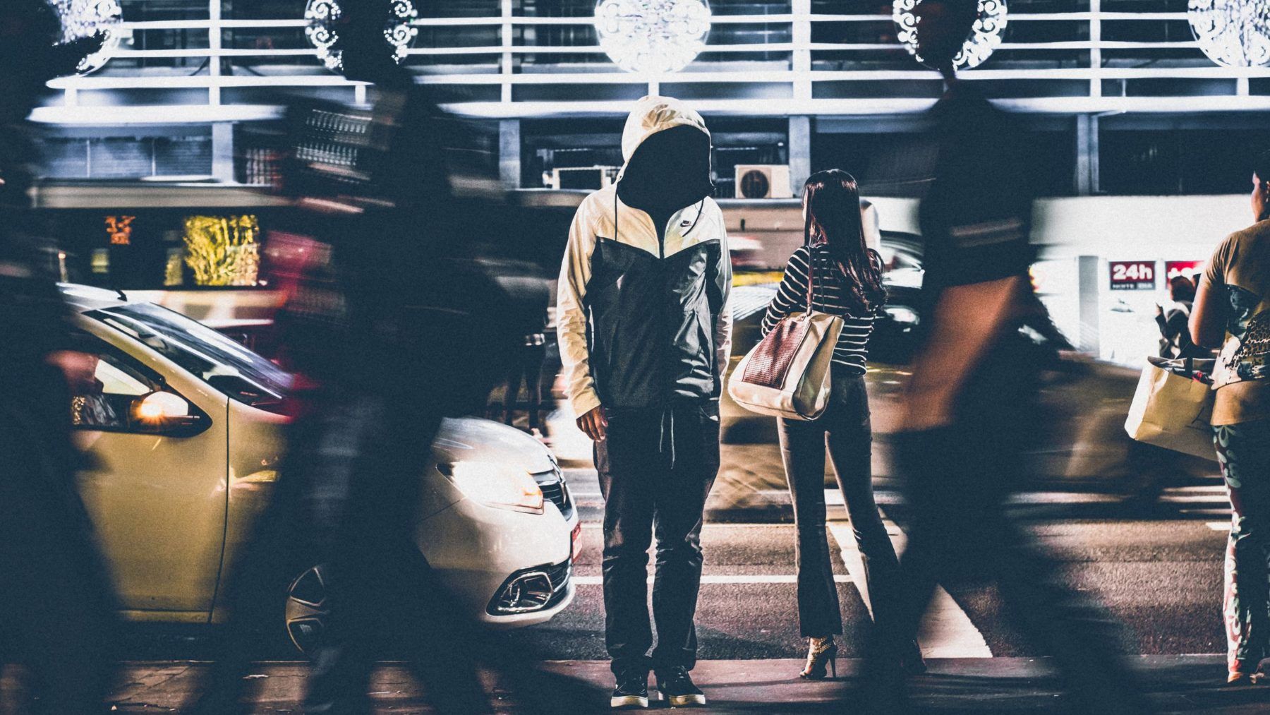 A person crossing a city street at night, seen from behind