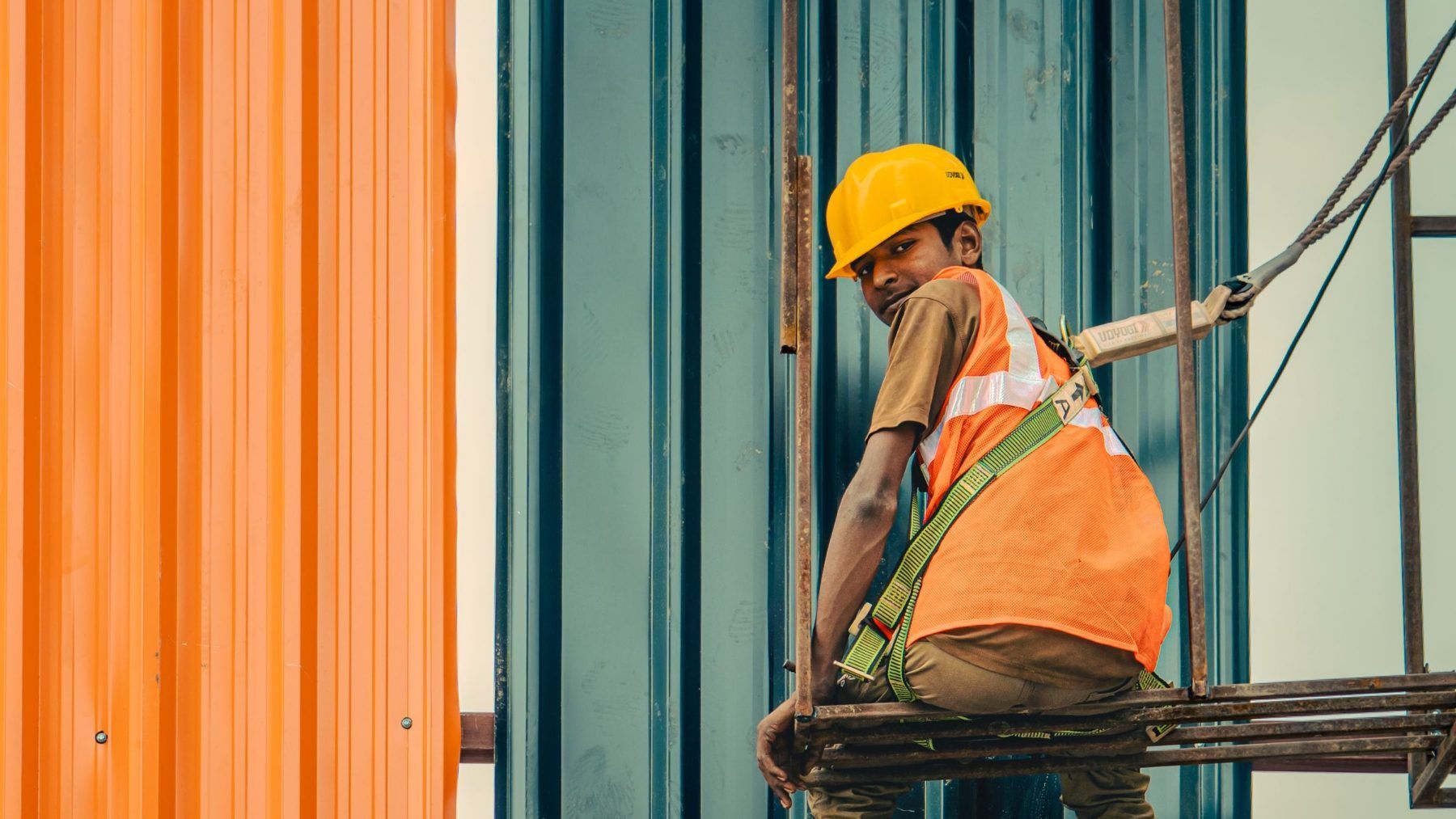 A construction worker carrying steel across a scaffold, looking back