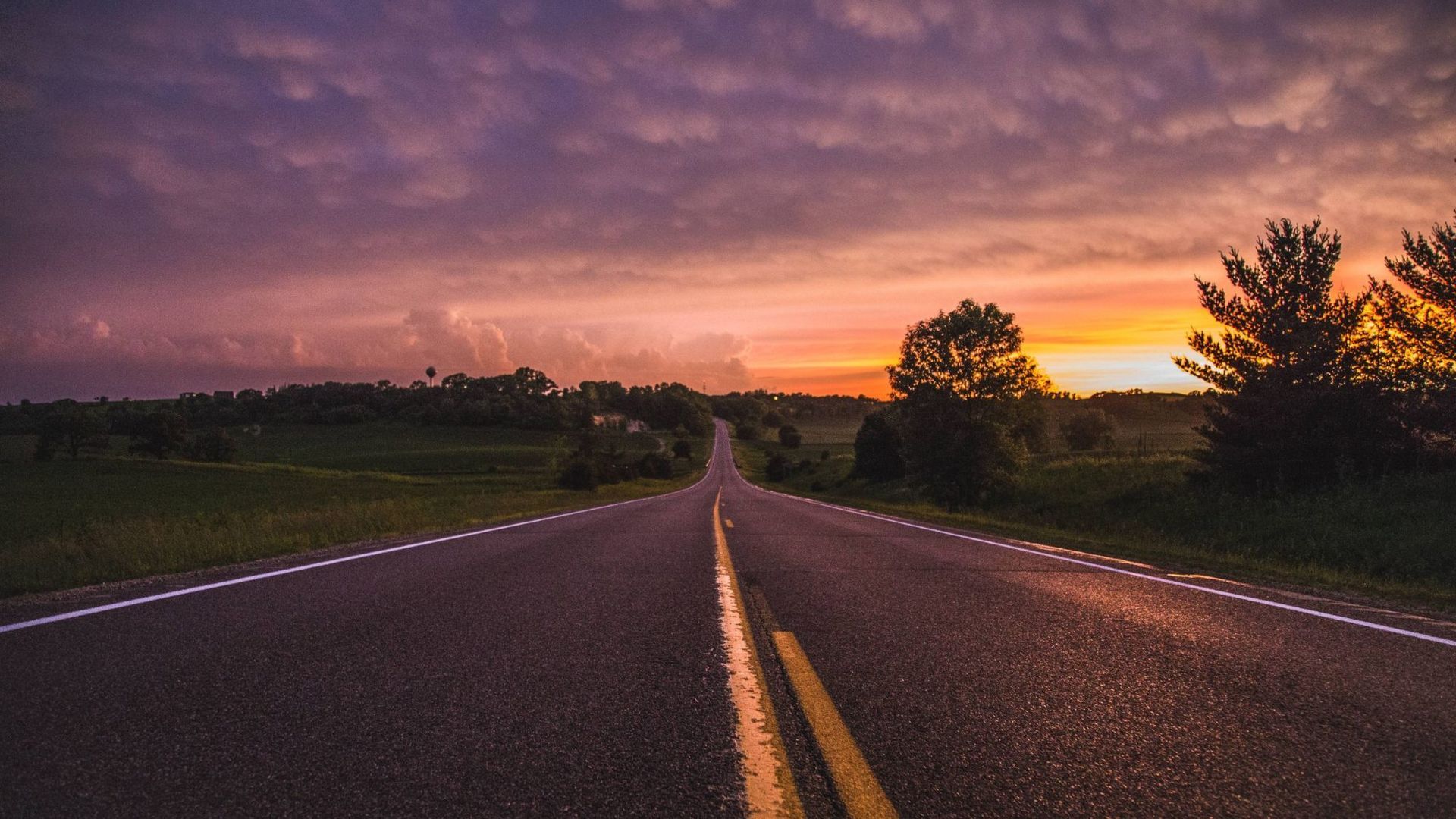 An empty two-lane road running to the horizon at first light