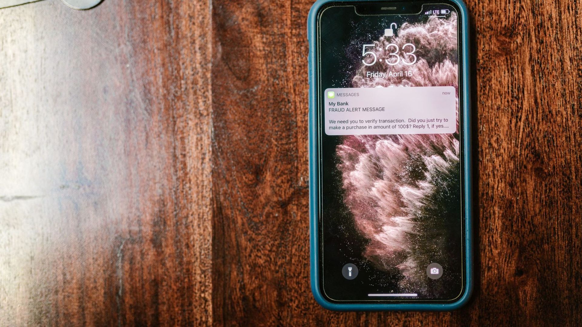 A phone lying face up on a dark wood table, one notification showing