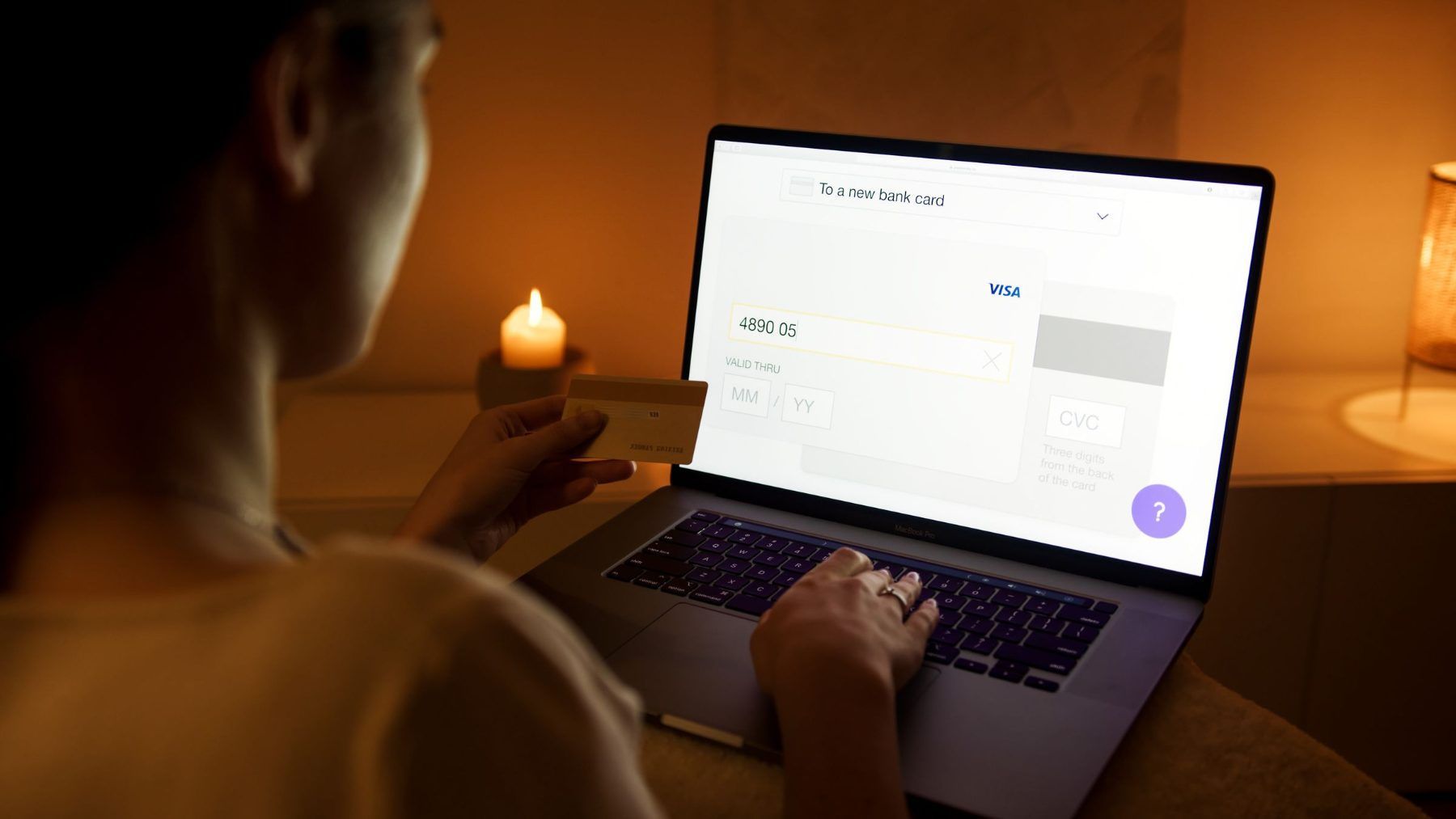 A person entering card details into a laptop by candlelight