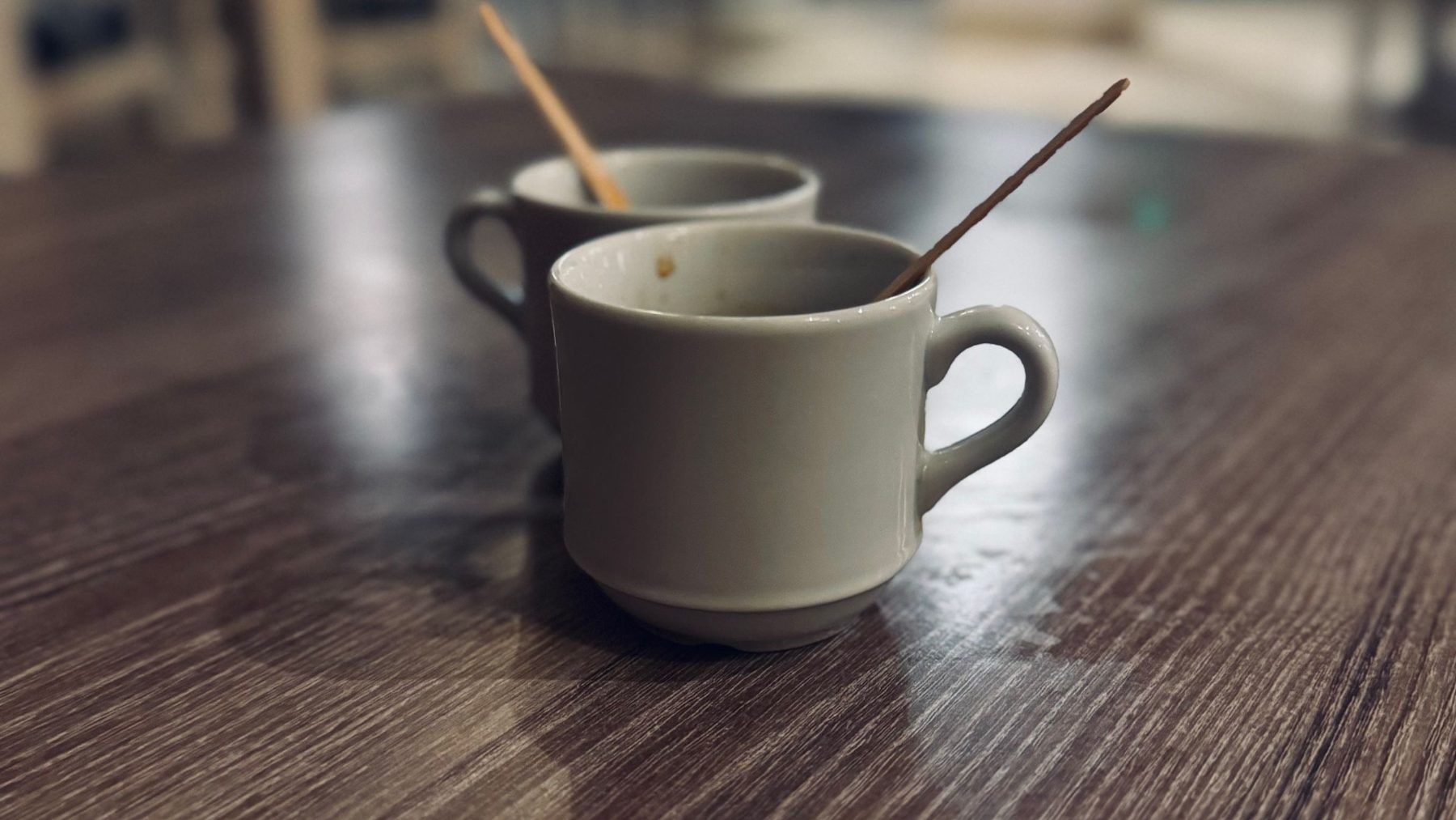 Two plain coffee cups on a dark wood table