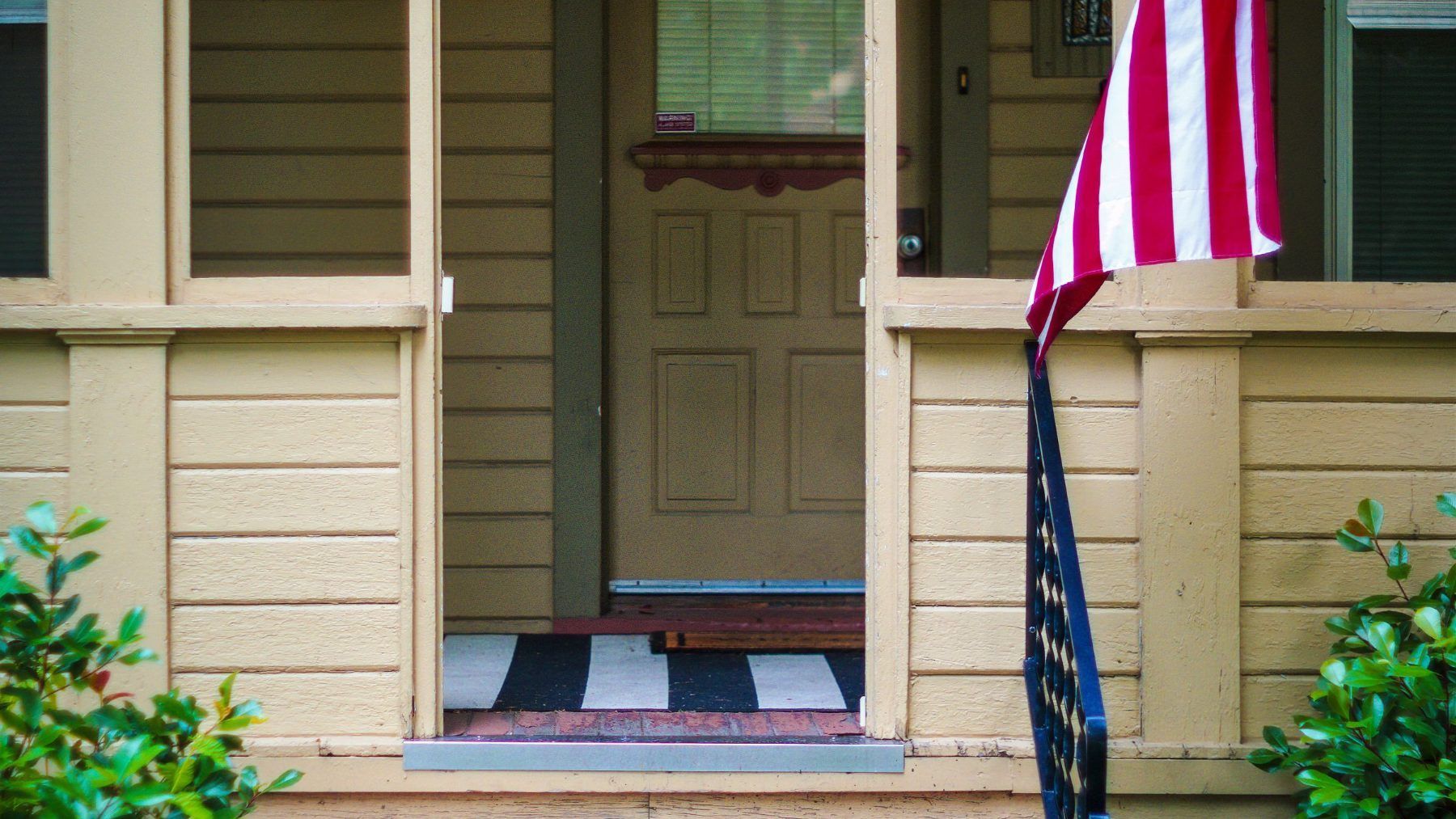 The front door and porch of a house with a flag beside it
