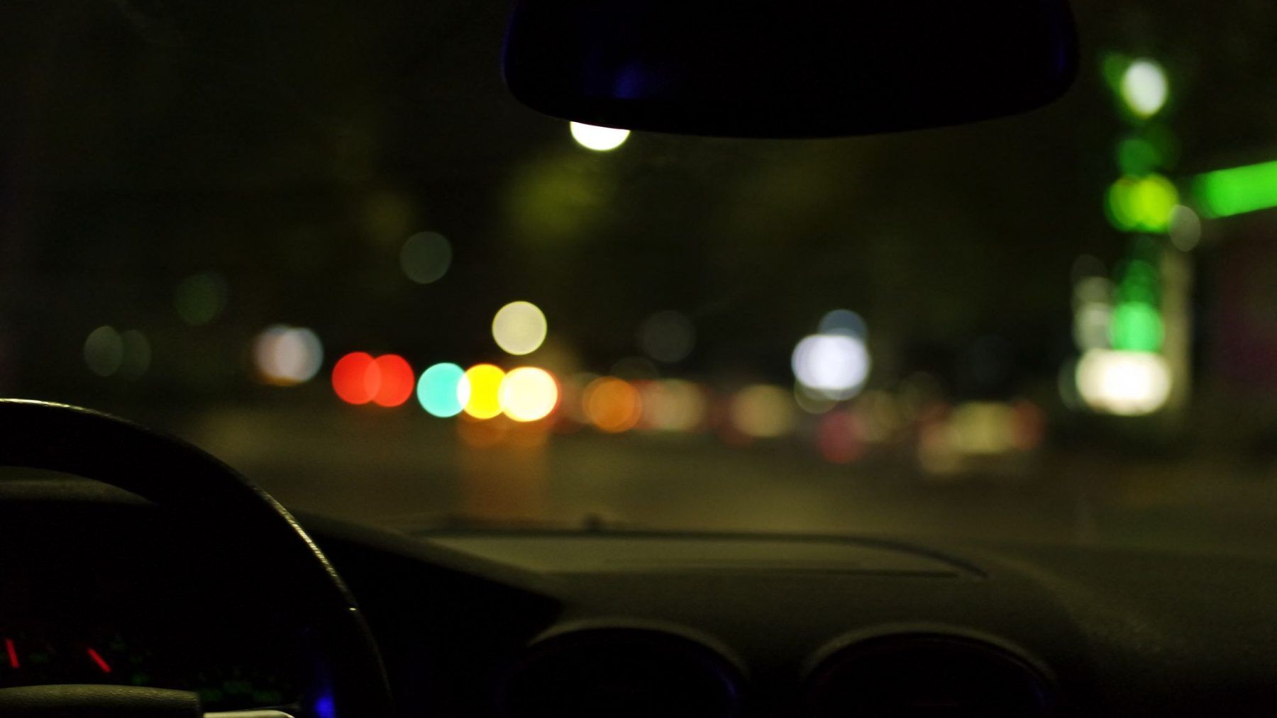 The view forward from inside a parked car at night, city lights out of focus beyond the windshield