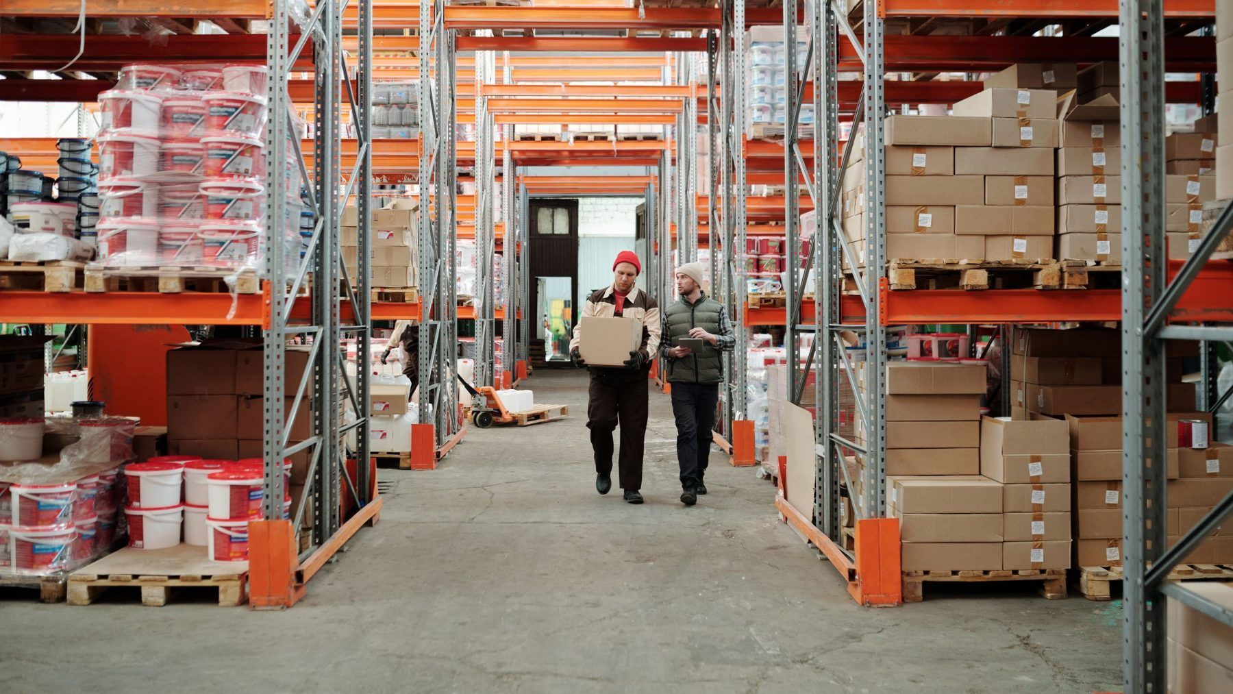 Two workers walking away down a warehouse aisle between racked pallets