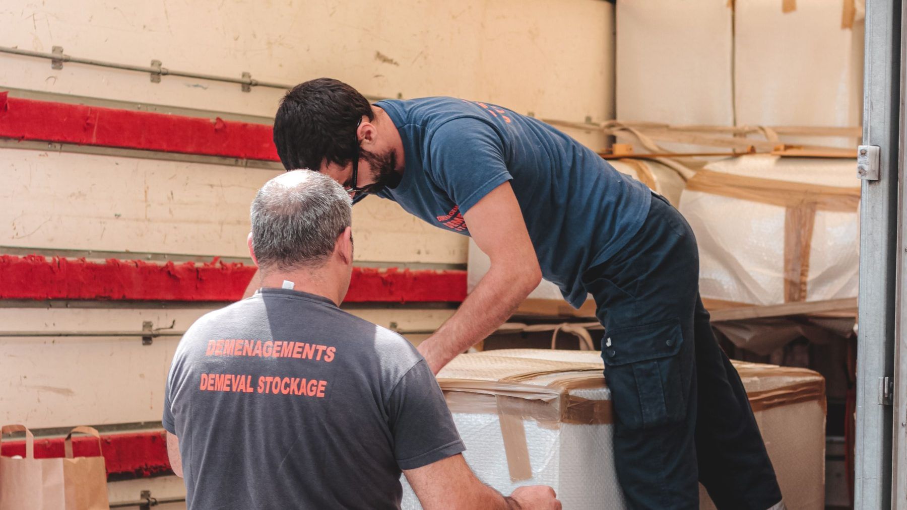 Two men loading a heavy crate into the back of a truck