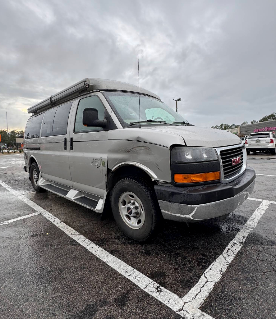 Silver passenger van parked in a wet parking lot under cloudy skies | Mike's Garage