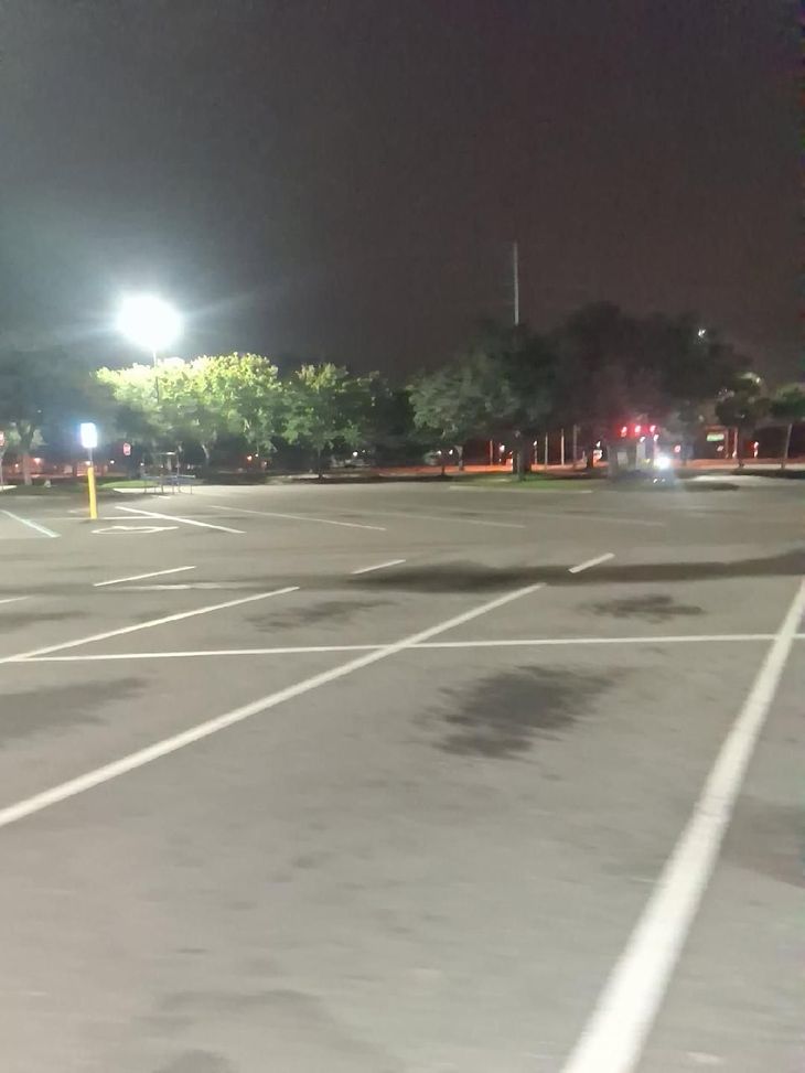 Empty parking lot at night with bright streetlights and trees in the distance