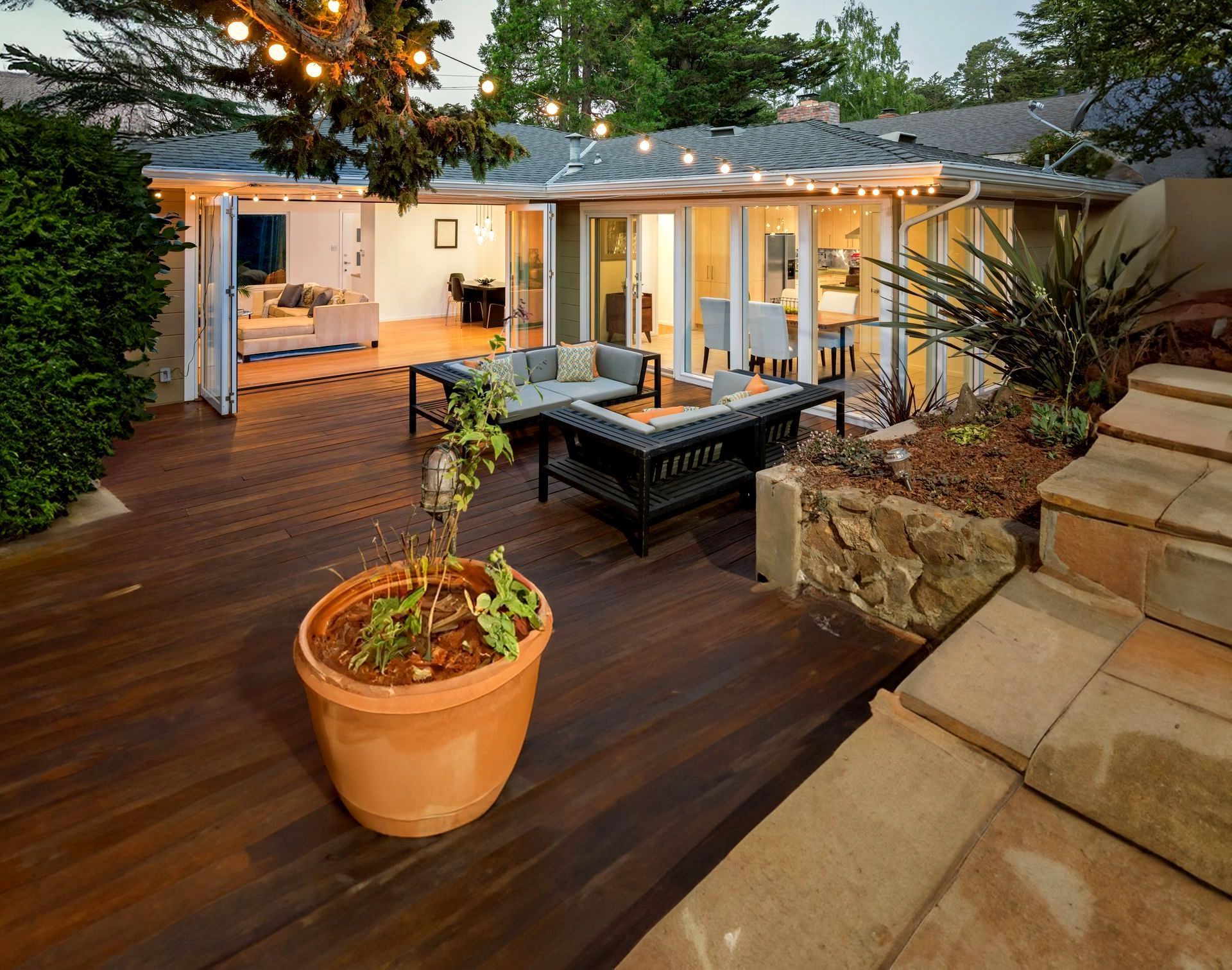 Terrasse extérieure en bois avec plante en pot, salon de jardin et patio ouvert baigné d'une douce lumière au crépuscule