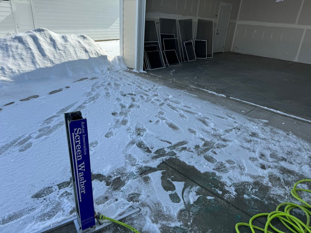 Snowy driveway beside open garage with stacked folding chairs and a blue signpost in the foreground