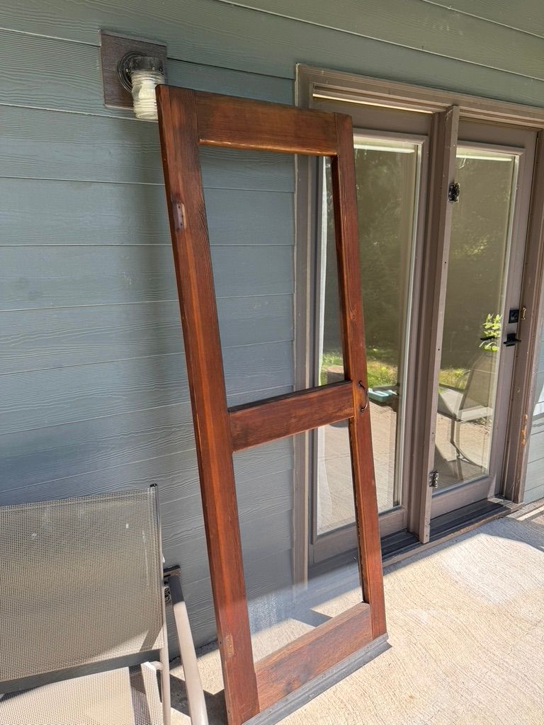 Tall wooden ladder-style frame leaning against a blue house wall beside a glass door.