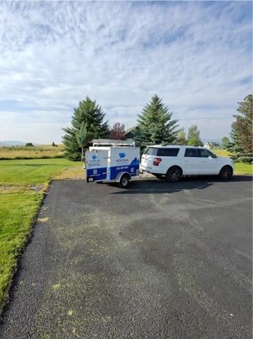 White SUV towing a blue-and-white trailer parked on an asphalt lot beside a grassy field under a cloudy sky