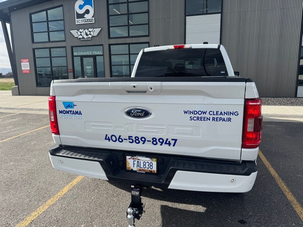White pickup truck parked outside a commercial building with phone number and company lettering on the tailgate