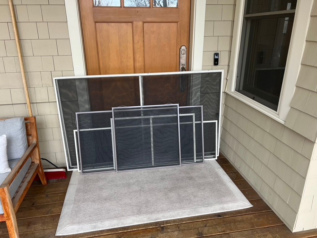Stacked window screens leaning against a house door on a small porch mat.