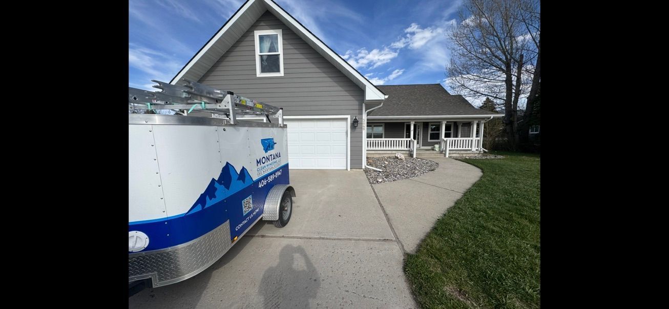 Gray house with a white garage, blue utility truck in driveway, and a gravel side path under a blue sky