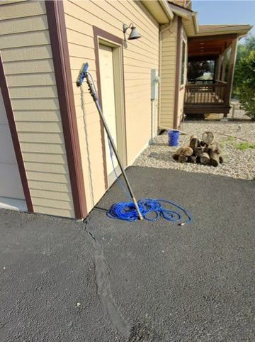 Blue hose reel beside beige house and garage, with coiled hose on gravel driveway.