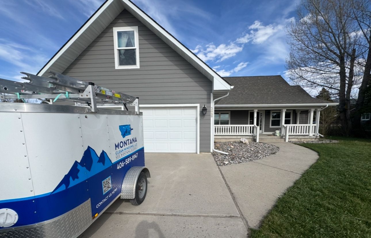 Blue and white utility trailer in a driveway beside a gray house with a garage and front porch.