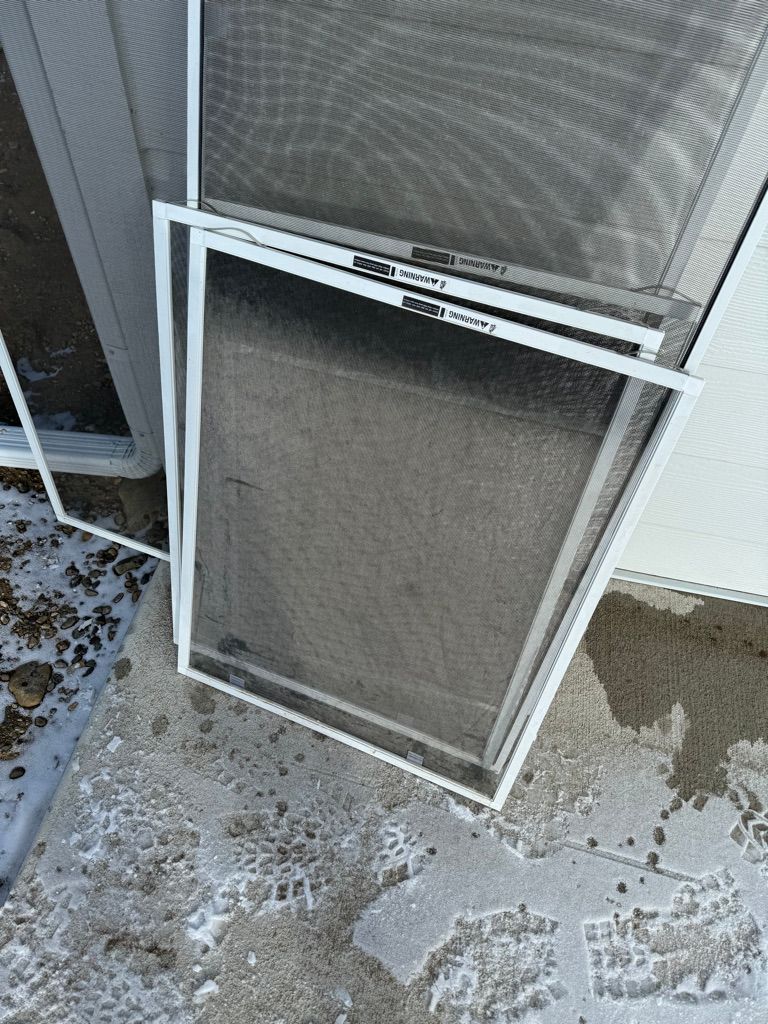 Two window screen panels leaning against a wall on a concrete patio with scattered debris