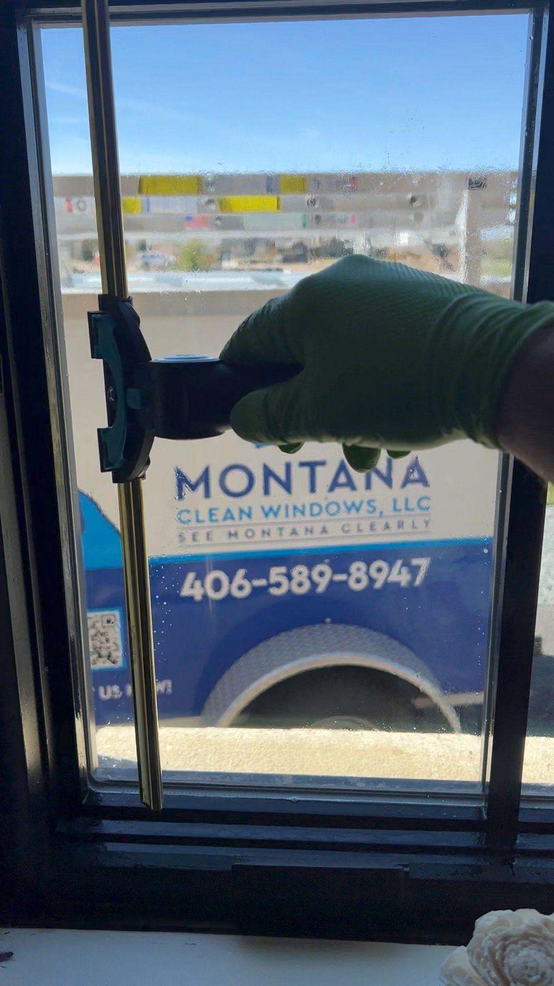 Gloved hand opening a glass door, with a Montana Clean Windows van visible outside.