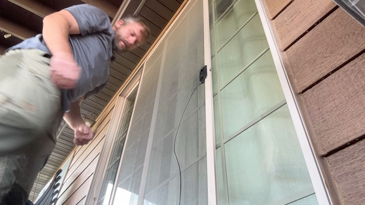 Man reaching up beside a window with a screen on a house exterior