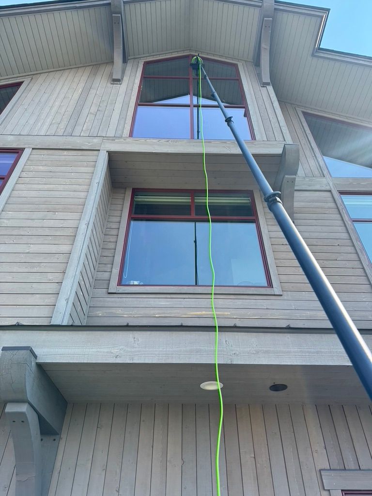 Person on a ladder painting a tall house exterior with a green rope hanging down