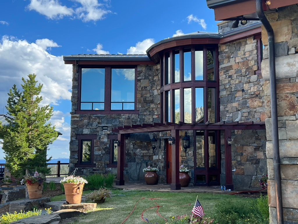 Stone house exterior with large windows, curved glass tower, and blue sky with clouds