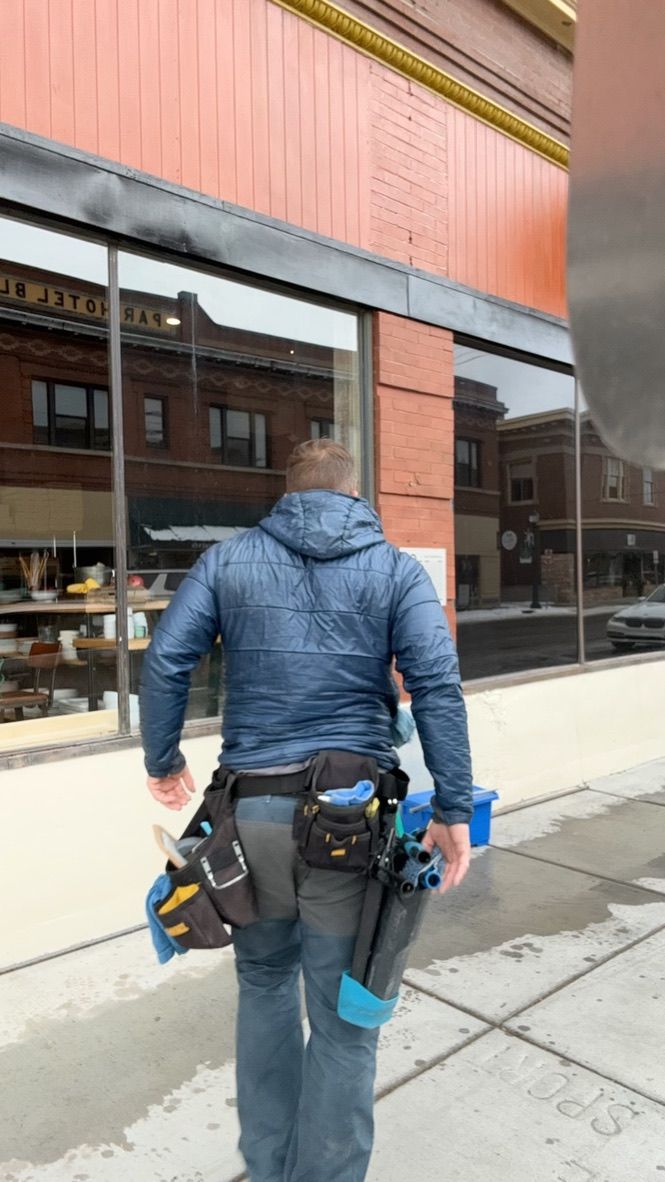 Person in a blue jacket and utility belt walking outside a building with large windows.