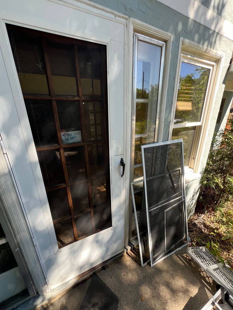 White screen door with removed screen leaning against a house beside a window and small porch.
