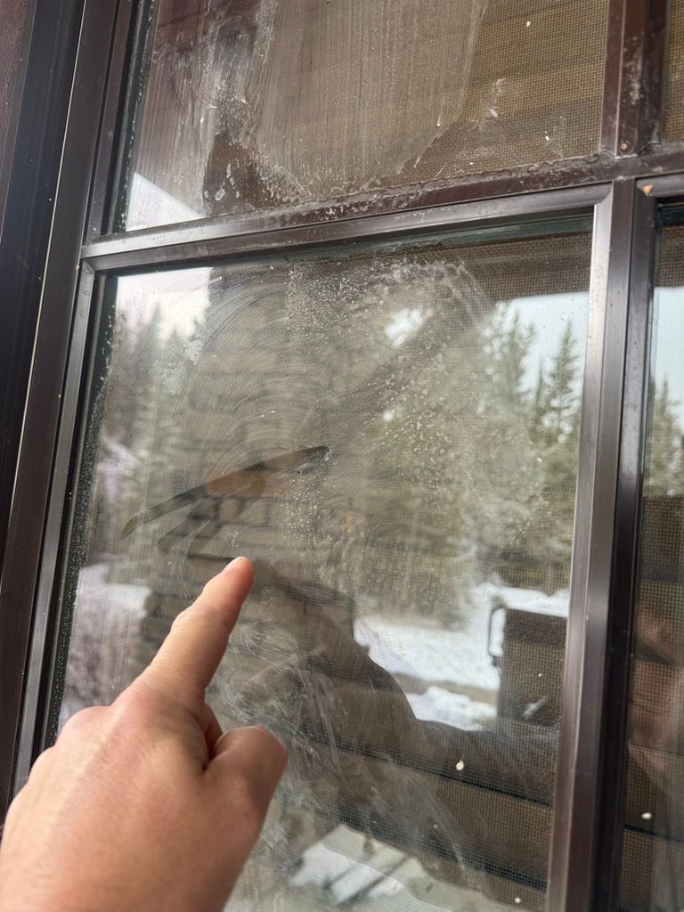 Hand pointing at a window pane with condensation and snowy trees outside