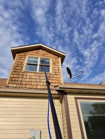Two-story beige house exterior with a dormer window, roof-mounted satellite dish, and blue sky with clouds above.