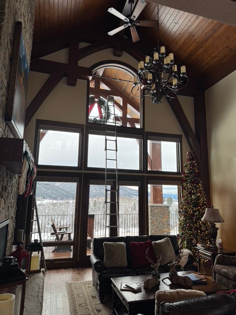 Rustic living room with vaulted wood ceiling, large windows, chandelier, and cozy seating by a stone fireplace