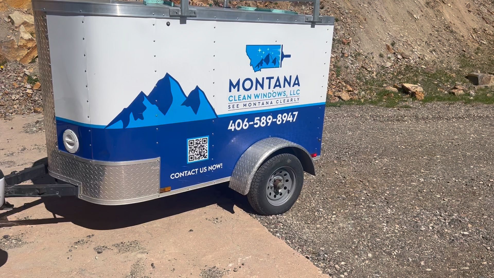 Montana trailer with blue mountain logo and phone number parked on gravel outdoors