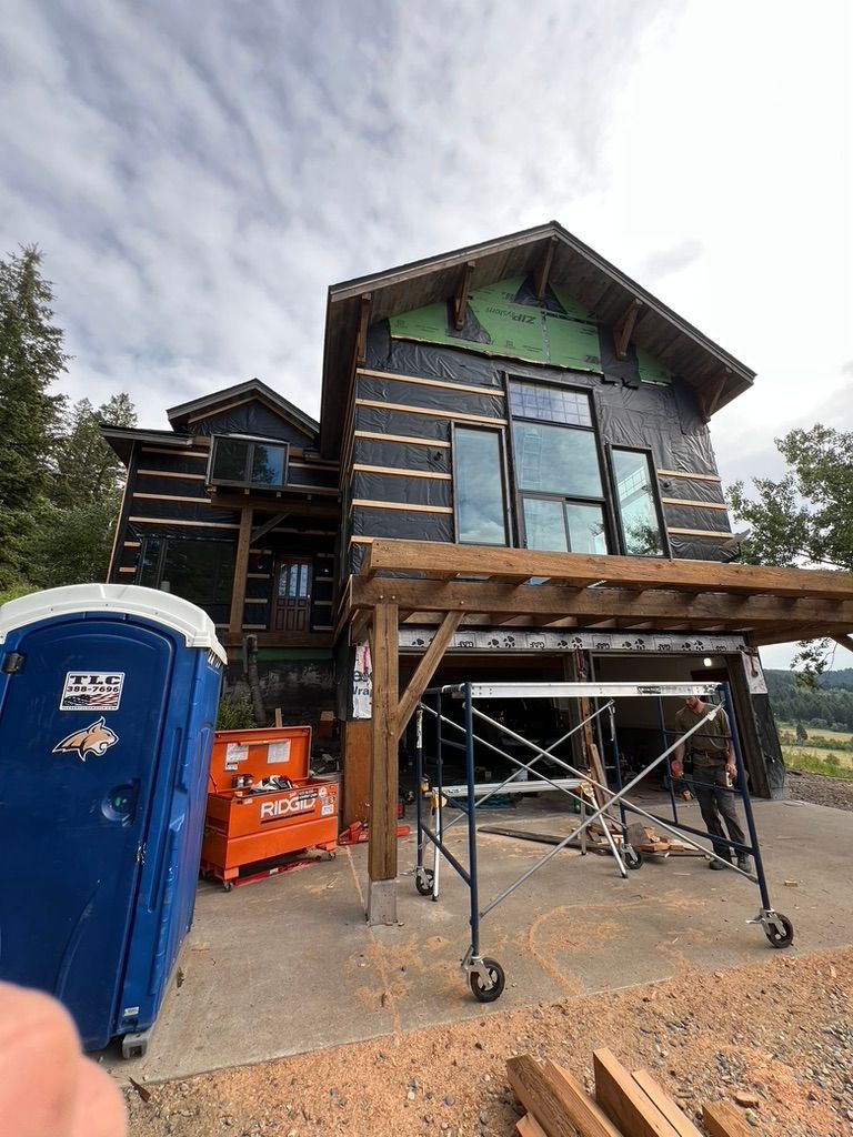 House under construction with scaffolding, a blue portable toilet, and orange equipment in front