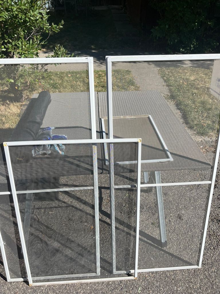 Several white-framed window screens leaning against a glass door outdoors on a patio.