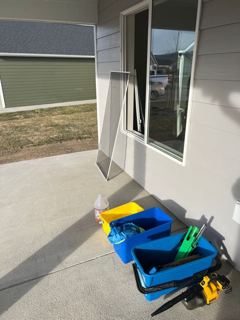 Blue bins and tools on a concrete patio beside a house window and wall.