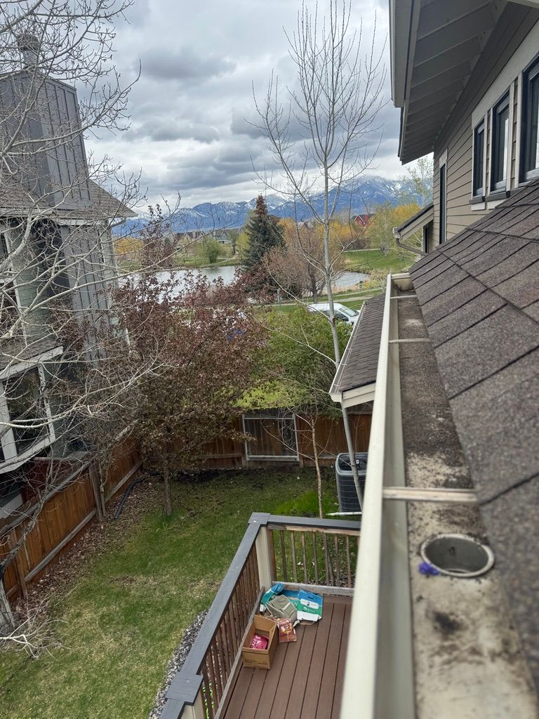 Backyard view from a rooftop, with neighboring houses, a small deck, bare trees, and mountains in the distance