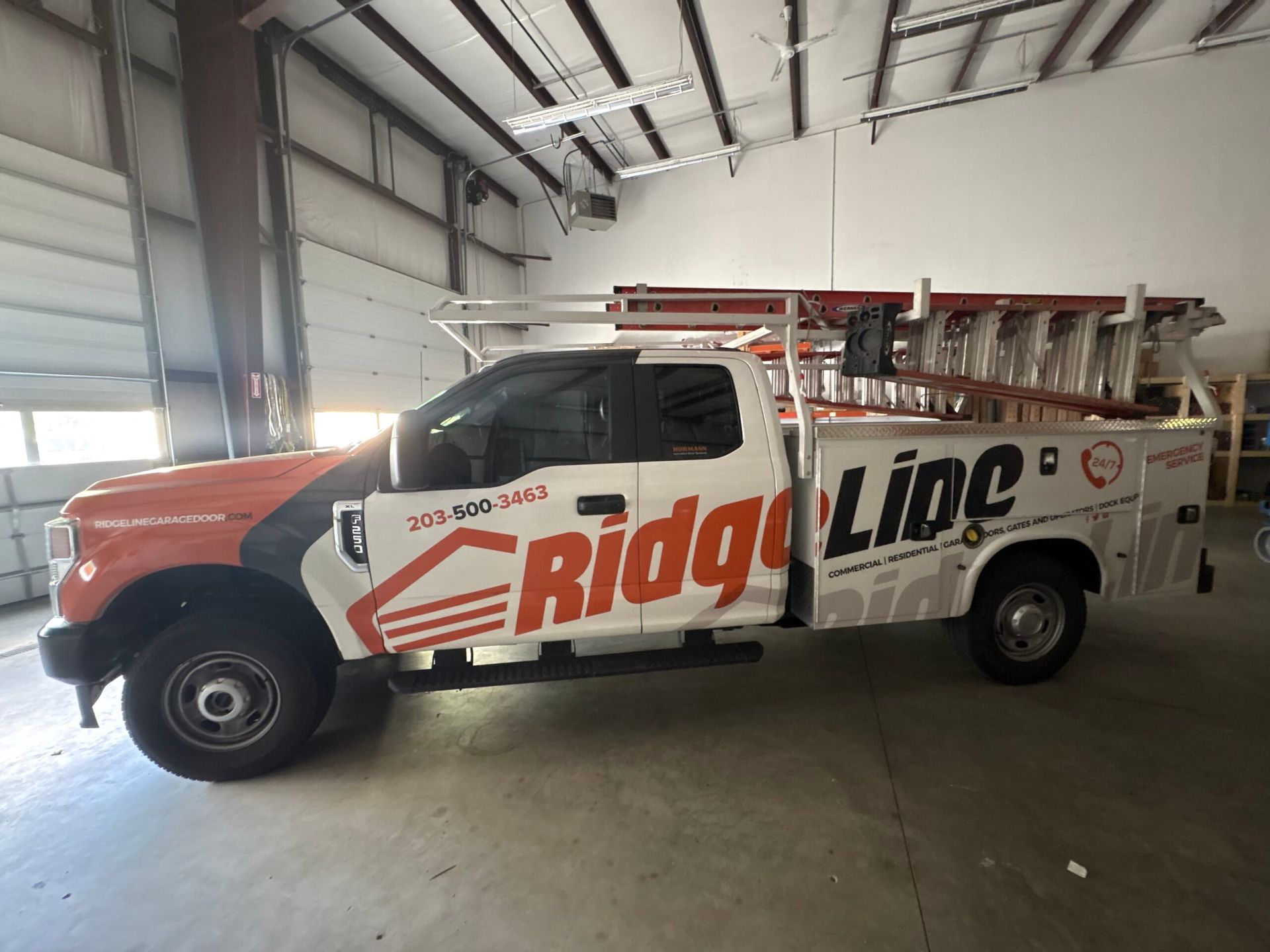 Ridgeline service truck parked inside a warehouse, white and red with ladders on top