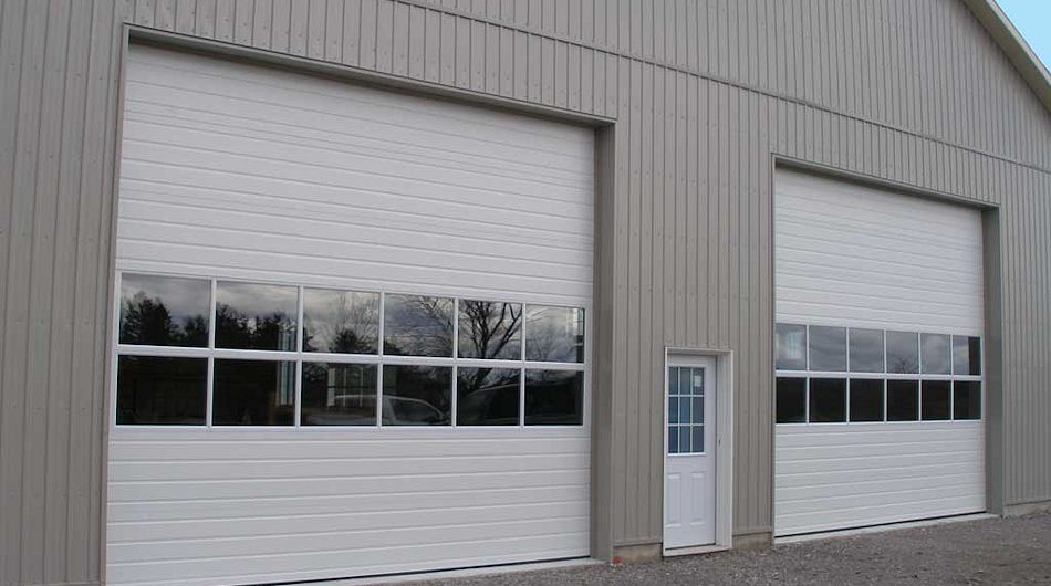 Two white garage doors on a gray industrial building with a small side door between them.