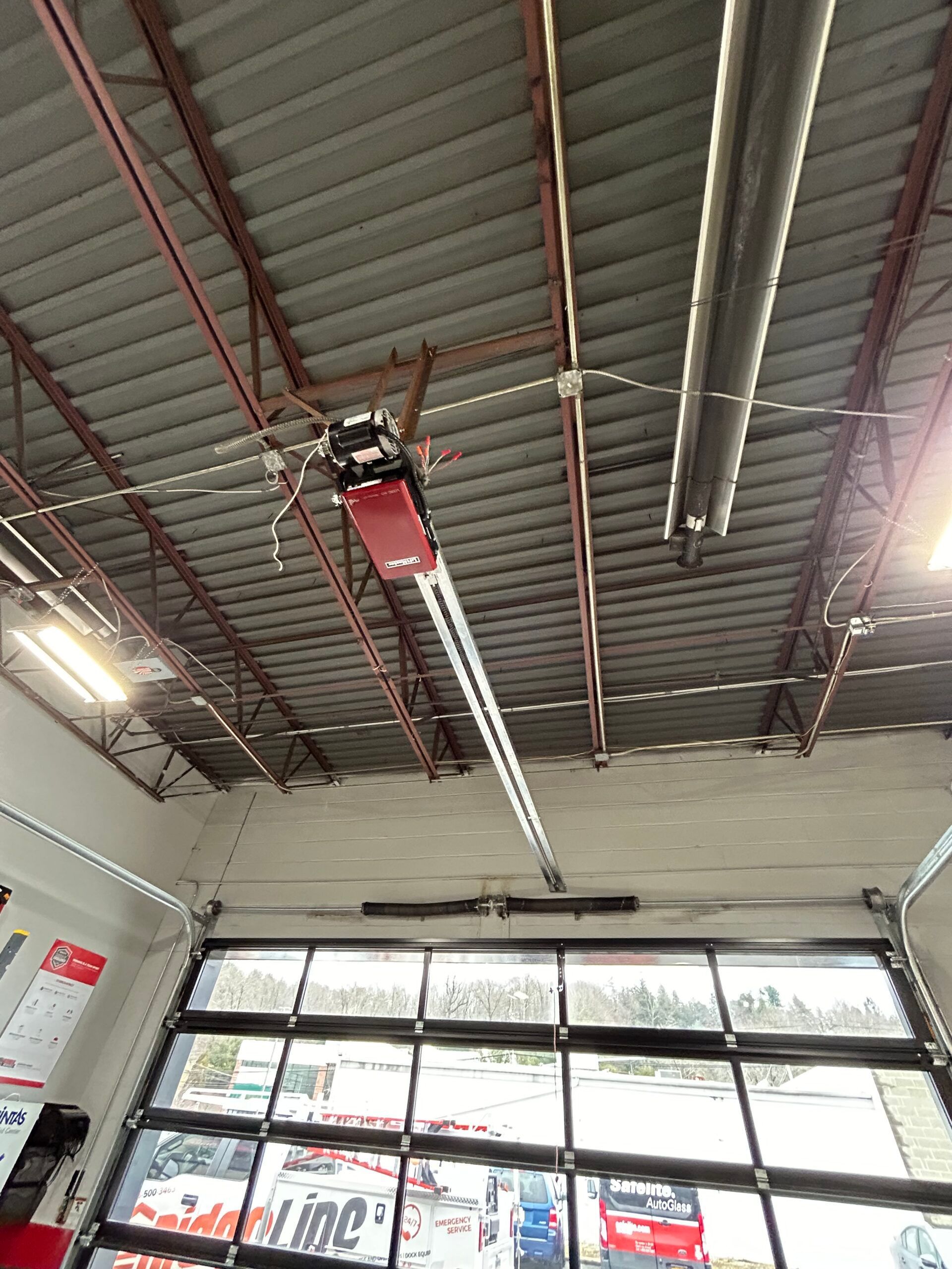 Ceiling-mounted red garage door opener in an industrial garage, with glass roll-up door below.