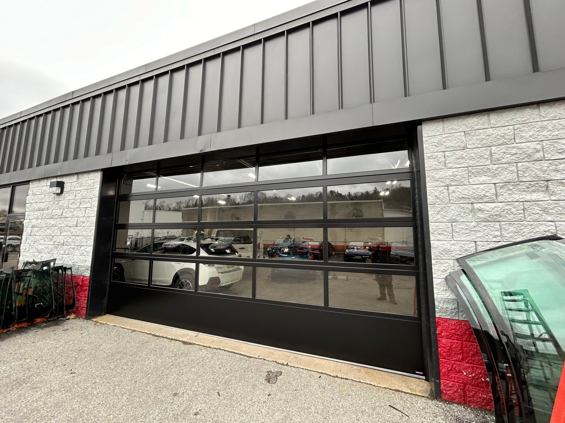 Modern building exterior with a large glass garage door and parked cars visible inside