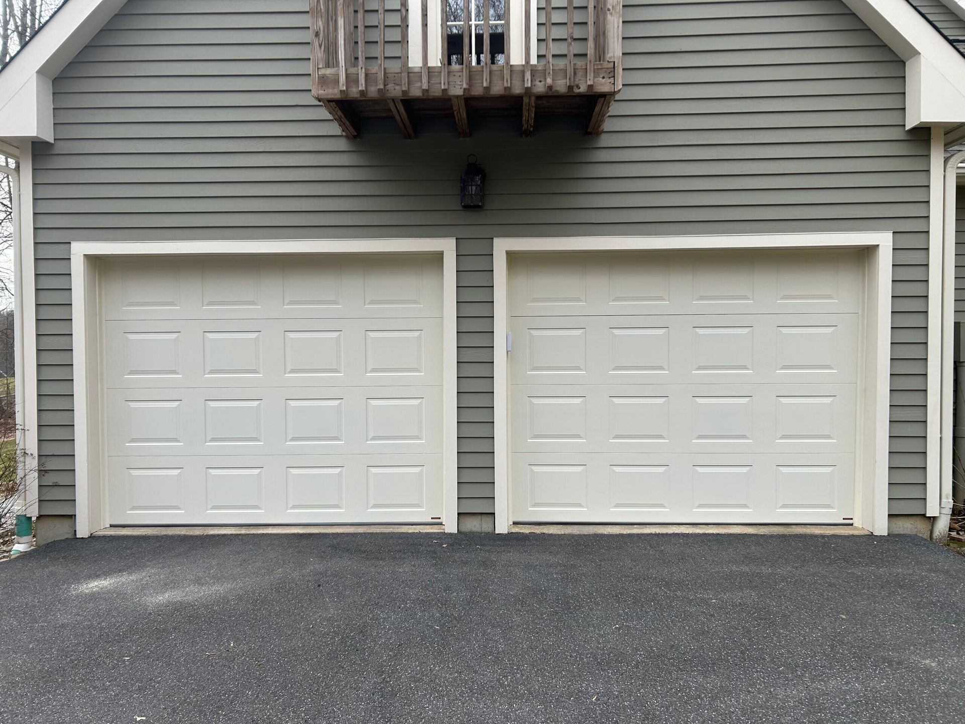 Two beige garage doors beneath a small wooden balcony on a gray house exterior