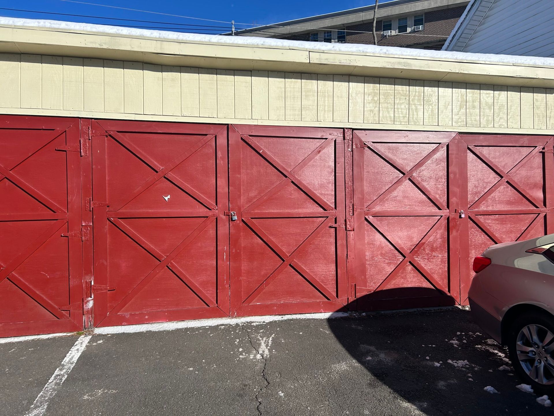 Red wooden garage doors beside a beige building, with part of a parked car in the foreground.