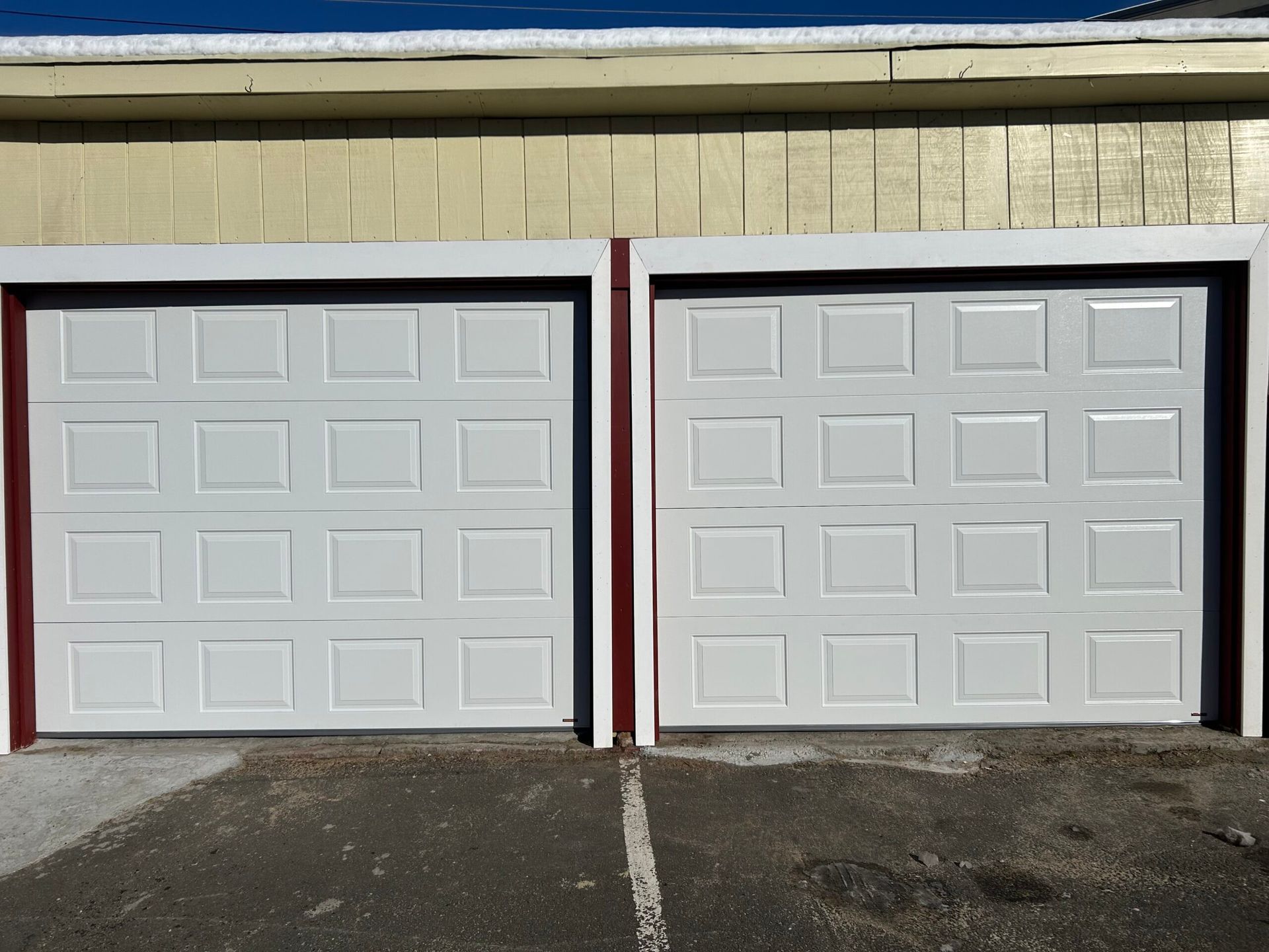Two white garage doors on a tan building, divided by a red trim center post.