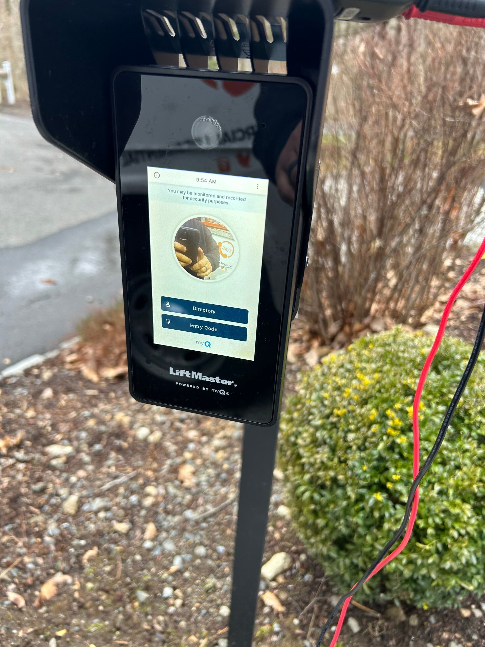 Parking meter with contactless payment sign beside a sidewalk and shrubs.