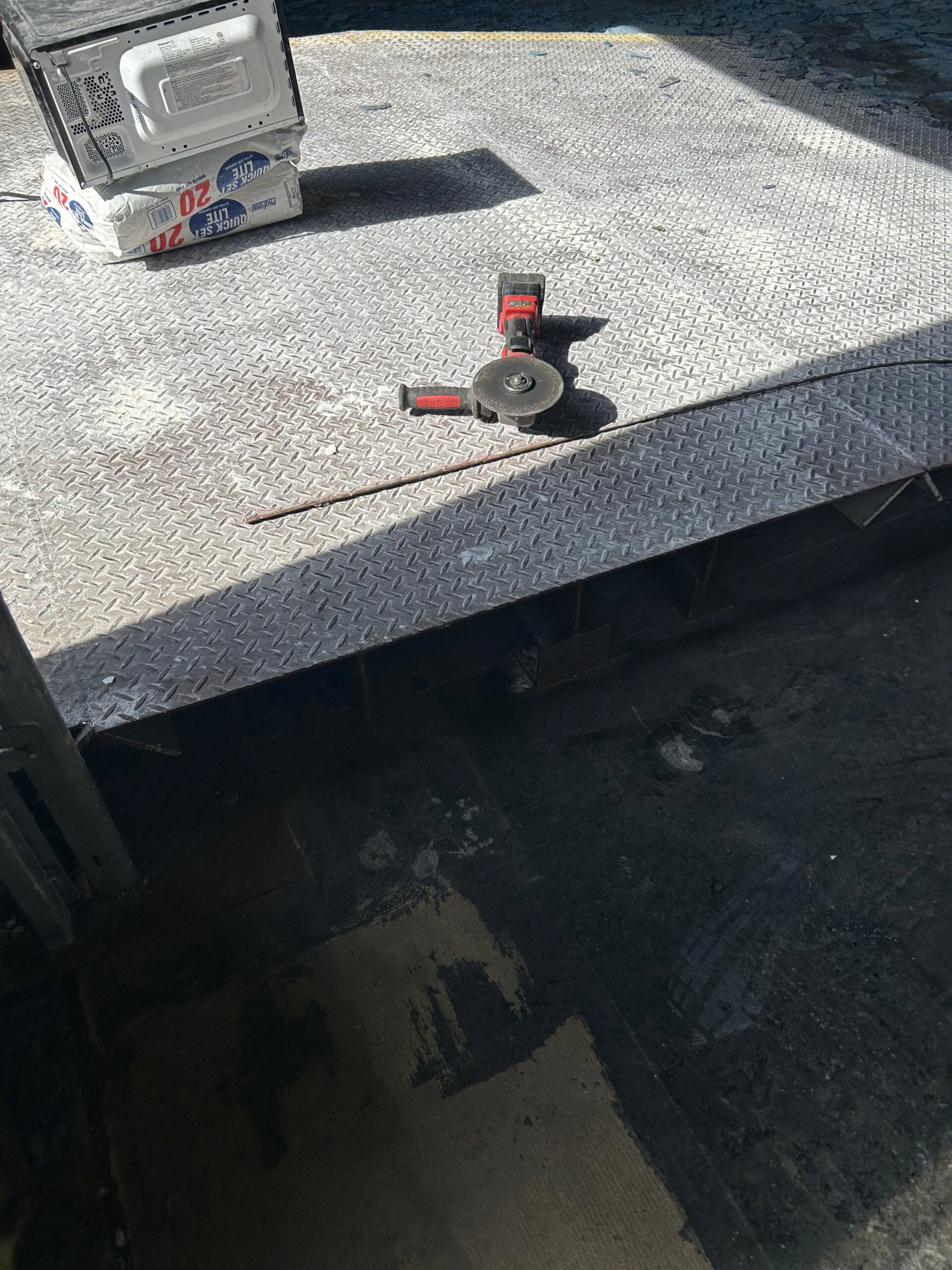 Roofing tools on a gray shingle roof, with a small box and a red-and-black tool near the edge.